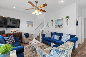 A living room with a ceiling fan, a TV, a staircase, and a blue sofa set.