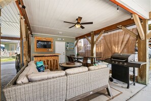 A covered outdoor seating area with a wicker sofa, a table, chairs, a grill, and a ceiling fan. - Ocean Lakes Luxe, 1 Min Walk to Beach and Fire Table! (Myrtle Beach)