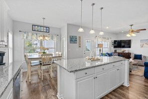 A kitchen with a large island, wooden chairs, a dining table, pendant lights, and a television in the living area. - Ocean Lakes Luxe, 1 Min Walk to Beach and Fire Table! (Myrtle Beach)