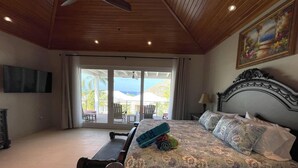 Une chambre dotée d’un grand lit, d’un banc en bois, d’une télévision et d’un balcon aménagé avec du mobilier d’extérieur.