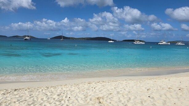 Une plage bordée d’une eau turquoise et cristalline, avec plusieurs voiliers amarrés au loin.