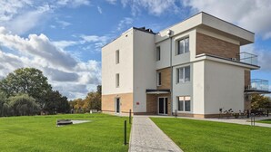 A modern multi-story residential building with a flat roof, large windows, and a small garden area with a paved walkway. - Stunning apartment in Insko with sauna (Insko)