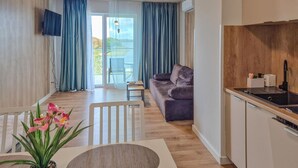 A modern living room with a sofa, a dining table with chairs, a kitchen area with a sink and stove, and a view of a balcony with curtains. - Stunning apartment in Insko with sauna (Insko)
