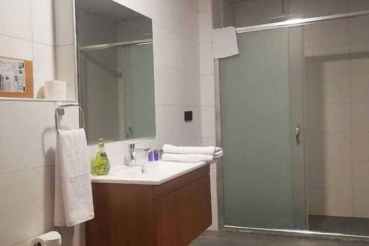 A bathroom with a glass shower enclosure, a white sink with a mirror above it, and a wooden vanity.