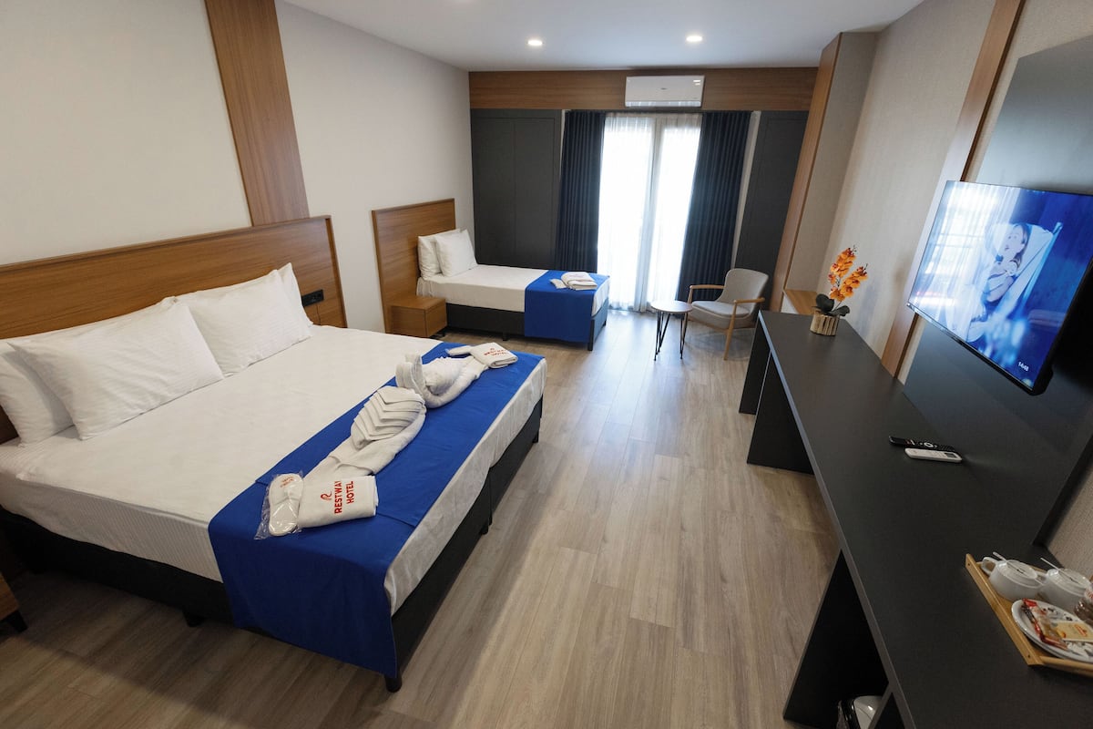 A hotel room with two beds, a desk, a TV, and a window with curtains.