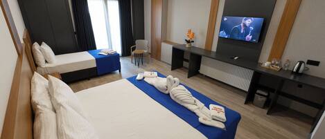 Quarto de hotel com uma cama grande, uma cama menor, uma escrivaninha, uma televisão e uma cadeira.