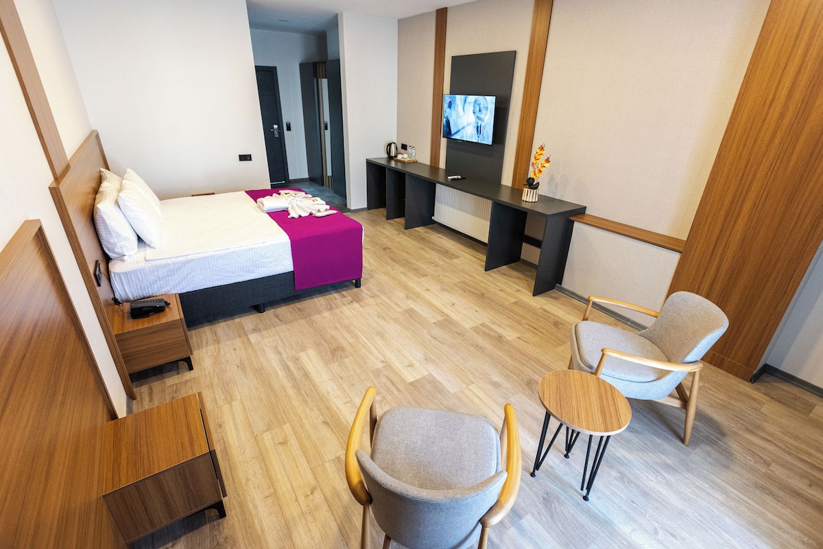 A modern hotel room with a bed, a desk, a TV, and two chairs.