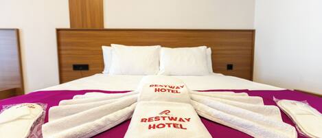 Una cama bien hecha con ropa blanca y toallas dispuestas en forma de abanico, exhibiendo el nombre "Restway Hotel".