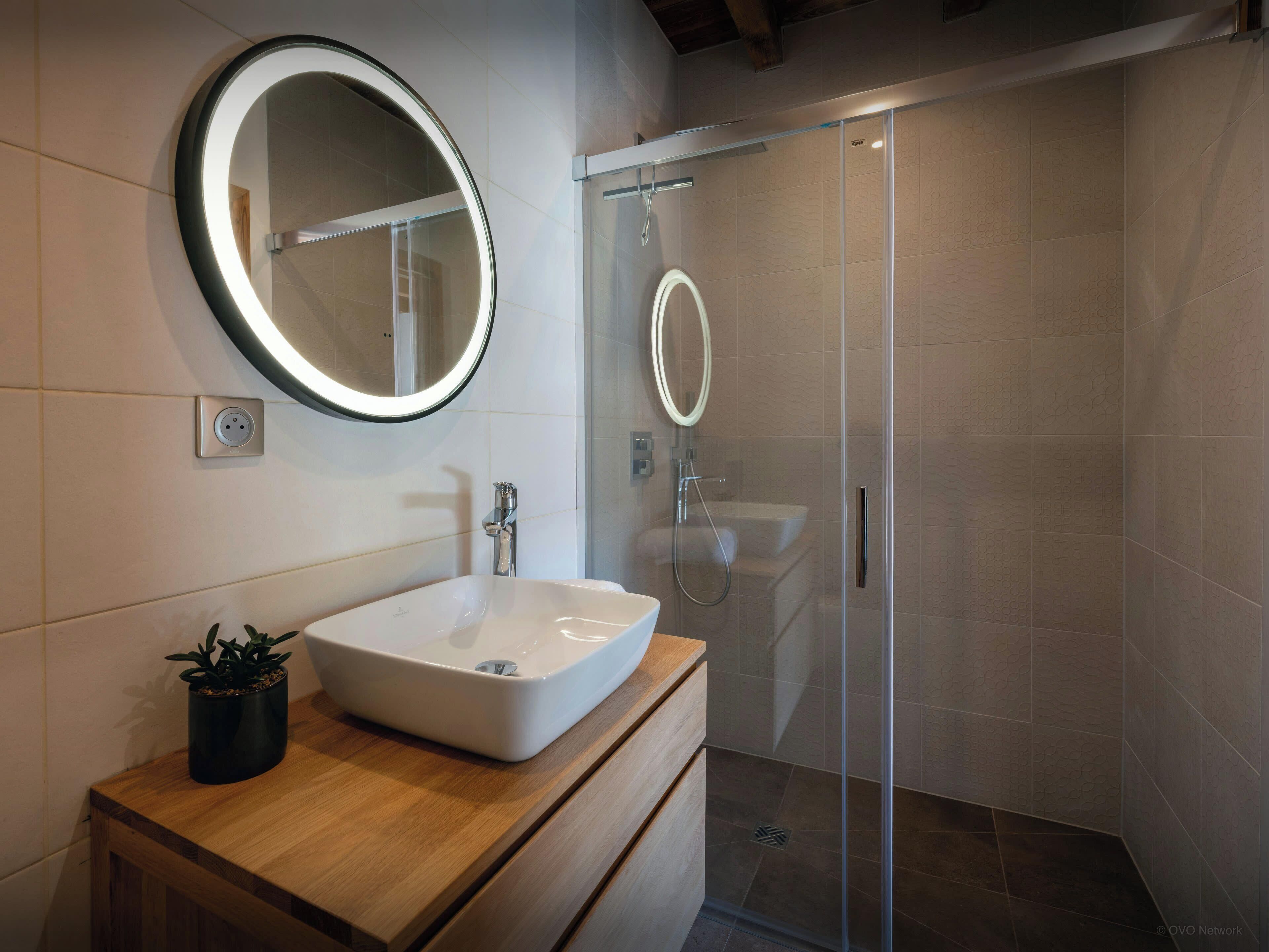 A modern bathroom with a large mirror, a white sink, and a glass-enclosed shower.