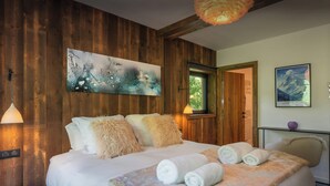 A wooden-paneled bedroom with a large bed, fluffy pillows, and a painting above it.