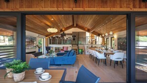 A modern interior with a wooden ceiling, a blue sofa, dining area, and a kitchen visible through an open door.