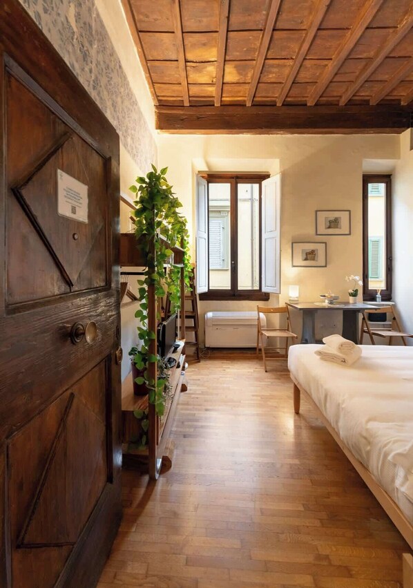 A room with a wooden door, a bed, a desk, a chair, and a radiator.