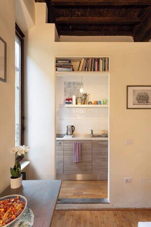 A kitchen with a wooden ceiling, a white countertop, and a sink. There is a bookshelf above the counter and a framed picture on the wall.