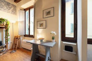 A room with a table, a radiator, a plant, and framed pictures on the wall.