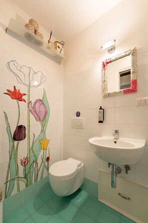 Une salle de bain comprenant des toilettes, un lavabo, un miroir et un mur orné de carreaux à motifs floraux.