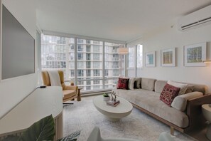 Ein modernes Wohnzimmer mit großem Fenster, einer Couch, einem Couchtisch und einem Sessel.