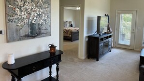 Ein Wohnzimmer mit einem Gemälde, einem dunklen Holzkonsole, einem Fernseher auf einem Standfuß und einer Tür mit Rollläden.