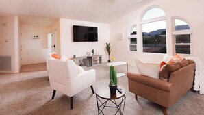 Un salon avec un canapé blanc, un canapé marron, une table basse ronde ornée d’un cactus et un téléviseur à écran plat fixé au mur.