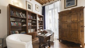 A room with a wooden bookshelf, a white armchair, a wooden table with a vase, and a large wooden cabinet. - Sauro River View By MMega (Firenze)