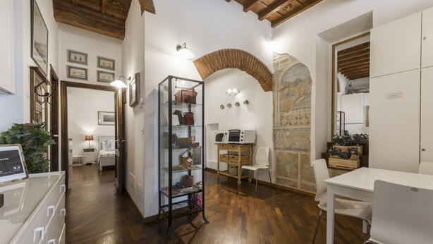 A room with wooden flooring, a white desk, a white chair, a glass display cabinet, and a stone wall with an arch. - Sauro River View By MMega (Firenze)