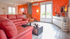 A living room with a red sofa, a brown leather chair, and a black coffee table. There is a TV on a white cabinet, and a window with blinds.