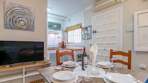A dining area with a wooden table set for four, a bottle of wine, and a television on a stand.