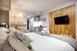 Ett modernt hotellrum med en stor säng, en vägg med träpanel som accent, en platt-TV och ett litet kök i bakgrunden.
