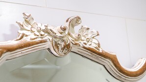 Ein Badezimmer-Spiegel mit aufwendiger Goldverzierung und weißem Hintergrund.