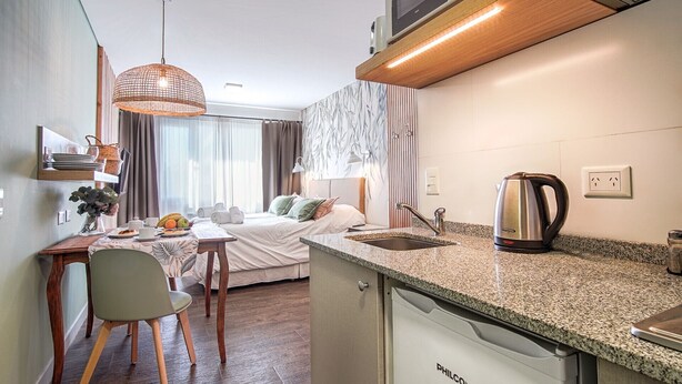 Habitación de hotel compacta con cama, mesita de noche y kitchenette.