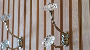 Un gancho montado en la pared con un tirador de cristal y una base metálica, sobre un fondo de madera a rayas.