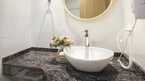 Un baño con lavamanos blanco, espejo redondo, secador de pelo y ducha.