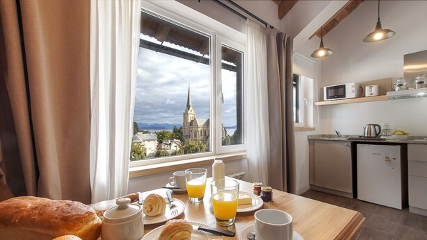 A breakfast table with croissants, orange juice, and a view of a church through the window.