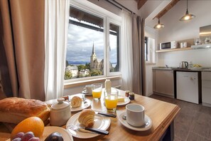 A breakfast table with croissants, orange juice, and a view of a church through the window.