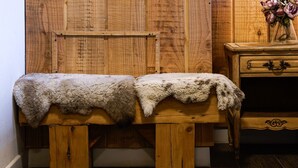 A wooden bench with a fur throw, a wooden cabinet with a vase of flowers, and a wooden wall.