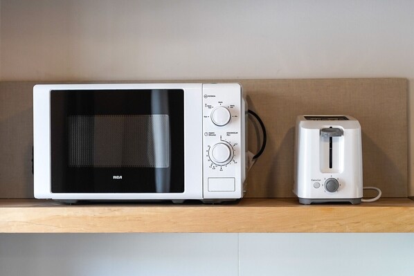 A microwave and toaster on a wooden shelf.