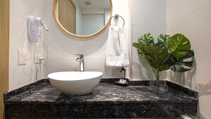 A bathroom with a white sink, a round mirror, a towel rack, a hairdryer, and a potted plant.