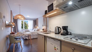 A compact kitchen with a microwave, coffee maker, and kettle, a dining area with a table and chairs, and a bed with a view of the outdoors.
