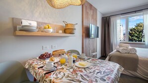 A well-lit room with a dining table set for breakfast, a TV mounted on the wall, and a window with curtains.
