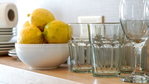 Un bol blanc contenant des citrons, posé sur une surface en bois, accompagné de verres transparents.