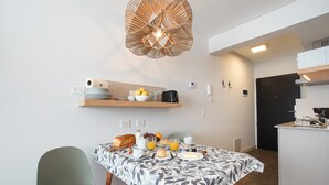 Une cuisine moderne avec un coin repas. La cuisine est équipée d’un four noir, d’un micro-ondes blanc et d’un plan de travail en bois. Le coin repas comprend une table recouverte d’une nappe à motifs de feuilles et deux chaises.