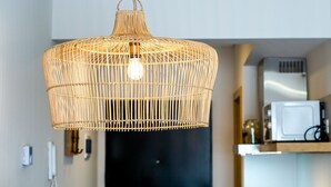 A woven pendant light fixture in a modern kitchen with a black cabinet and a white microwave on the counter.