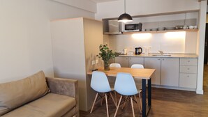 A compact kitchen with a microwave, toaster, and kettle. There is a dining table with two chairs and a sofa in the living area.