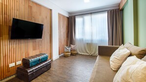 Ein Wohnzimmer mit Flachbildfernseher an einer Holzwand, einer Couch und einem Fenster mit Vorhängen.