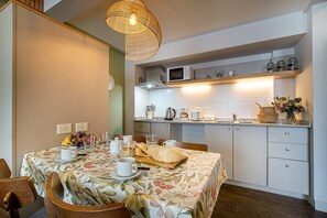 Un coin repas avec une table dressée pour deux personnes, un four à micro-ondes placé au-dessus du comptoir et un luminaire suspendu.