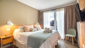 A neatly arranged hotel room with a bed, bedside tables, a chair, and a TV mounted on the wall. - Mutisia flat with terrace and lake views in Bariloche (San Carlos de Bariloche)