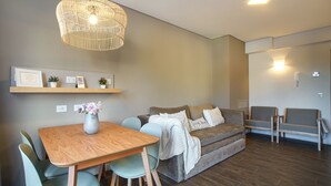 A modern living room with a wooden dining table, light blue chairs, a grey sofa with a white throw blanket, a wicker pendant light, and a small shelf with framed certificates and potted plants. - Mutisia flat with terrace and lake views in Bariloche (San Carlos de Bariloche)
