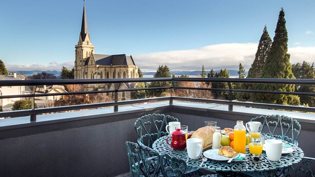 A balcony with a table set for breakfast, overlooking a church and mountains. - Mutisia flat with terrace and lake views in Bariloche (San Carlos de Bariloche)