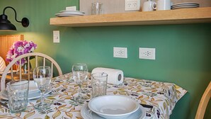 Een eethoek met een tafel voor vier personen, een houten plank erboven met borden en bekers, en een wandlamp.