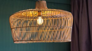 Een hangende geweven lamp met een gloeilamp erin, bevestigd aan het plafond.