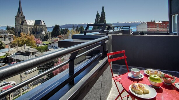 Een balkon met een ontbijttafel, met uitzicht op een kerk en bergen.
